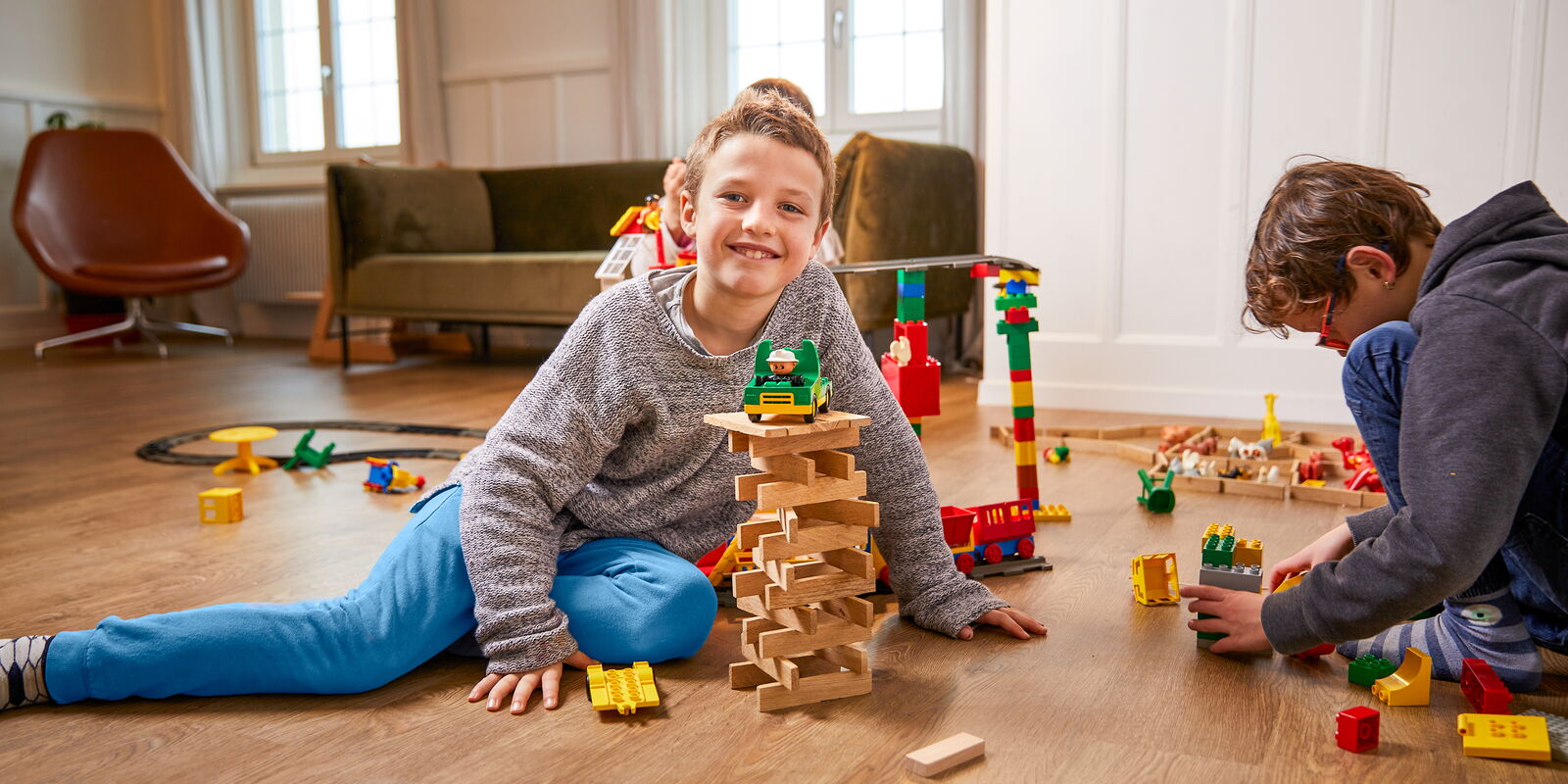 Ein Junge sitzt in einem Raum und spielt mit Bauklötzern; neben ihm spielt ein zweiter Junge.
